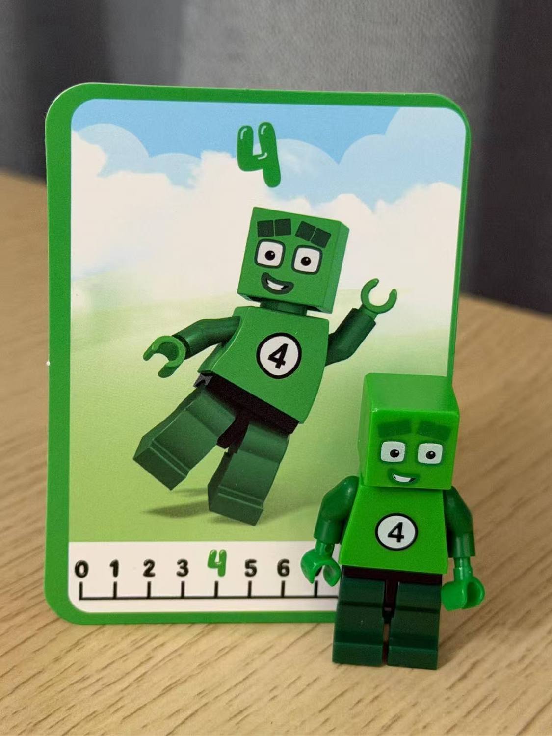 Numberblocks building blocks toy set featuring green character number 4 with matching card on a wooden surface.