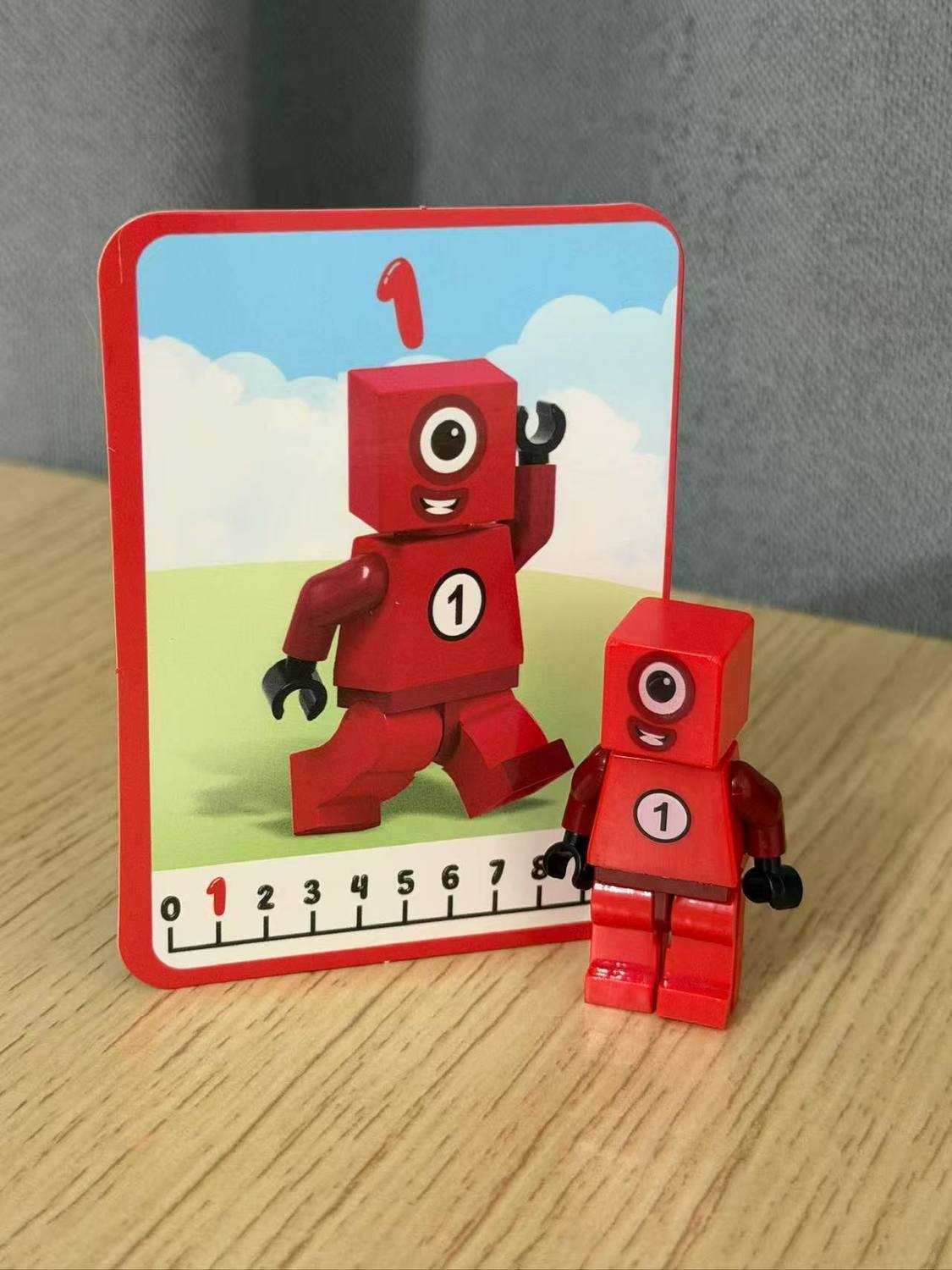 Numberblocks building blocks toy set featuring a red Number 1 character and a matching card on a wooden surface.