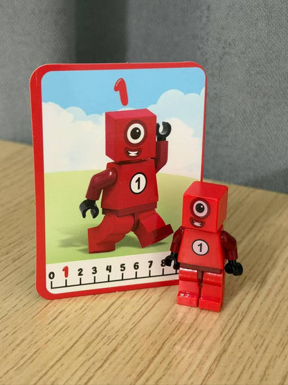 Numberblocks building blocks toy set featuring a red Number 1 character and a matching card on a wooden surface.